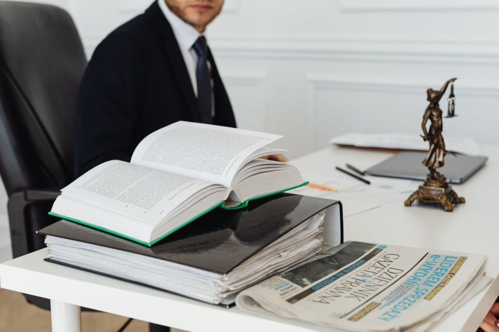 book-and-binder-on-a-desk-7876088 A lawyer sitting at a desk with legal books, documents, and a newspaper, embodying professionalism.